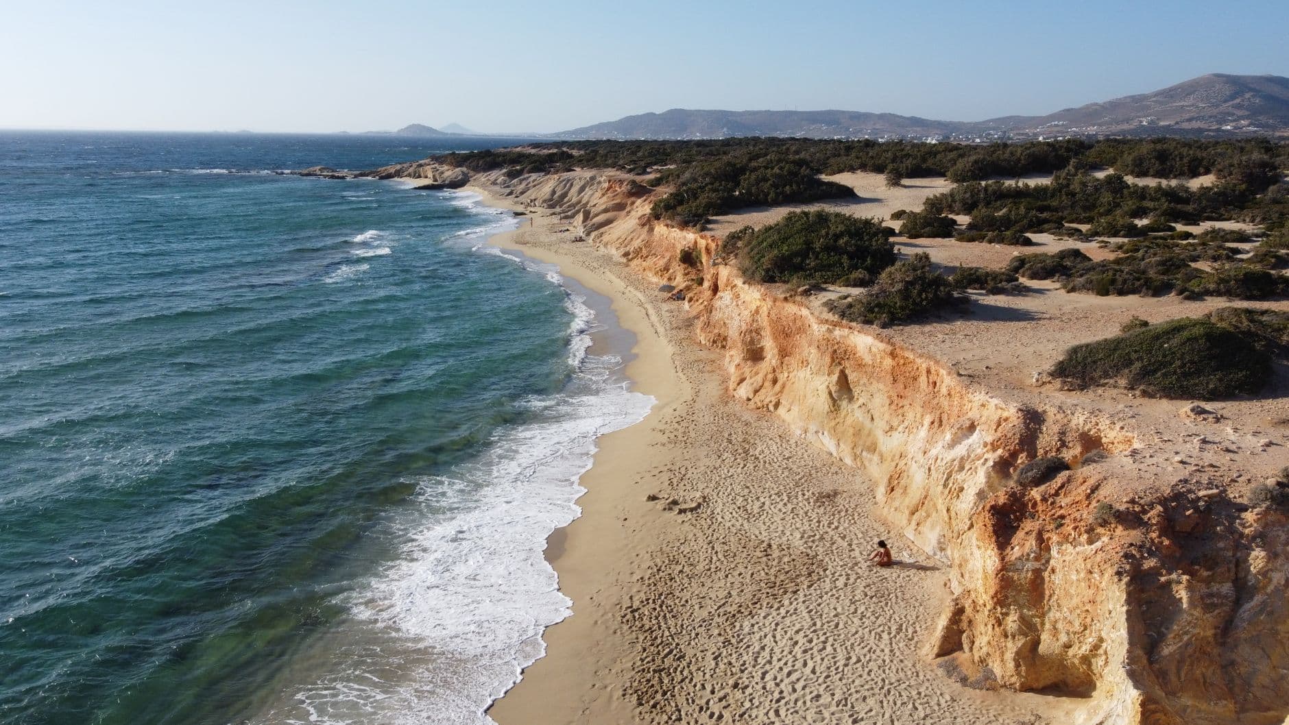 Stunning aerial view of Naxos beach with rocky cliffs and clear blue sea under sunny skies in Greece.